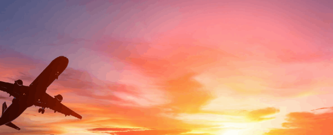 An aeroplane flying across a vivid orange and pink sunset sky.